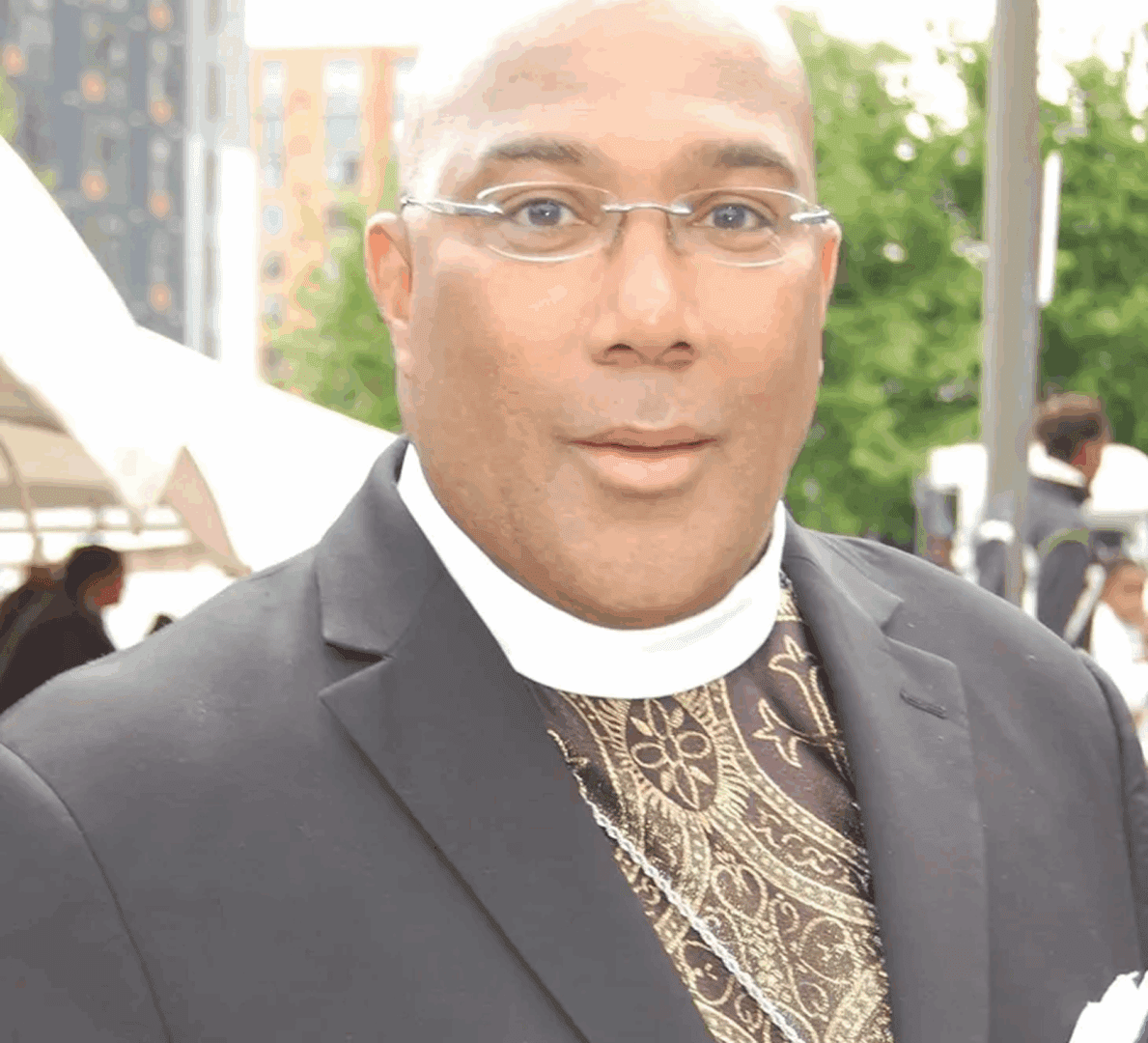 Man in suit and clerical collar outdoors.